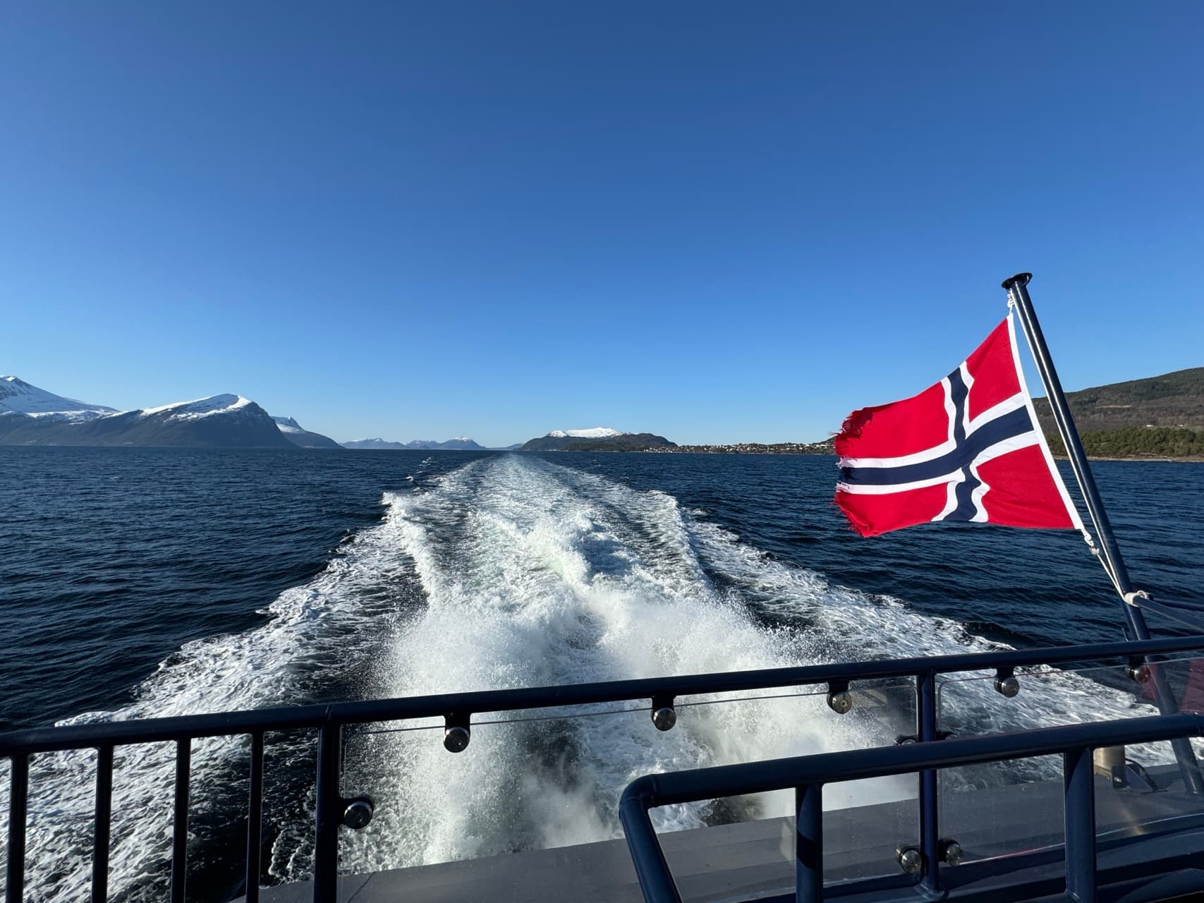 Norwegian boat cuts through the fjords under a blue sky