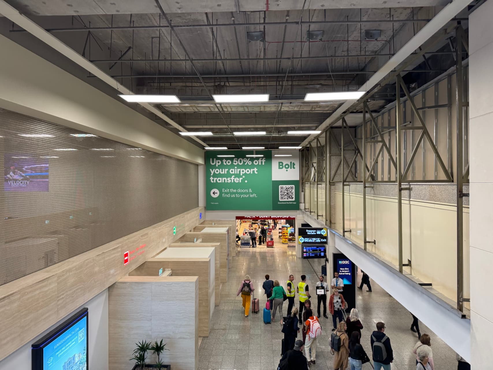 Busy arrival hall at Malta Airport with travelers and signage.
