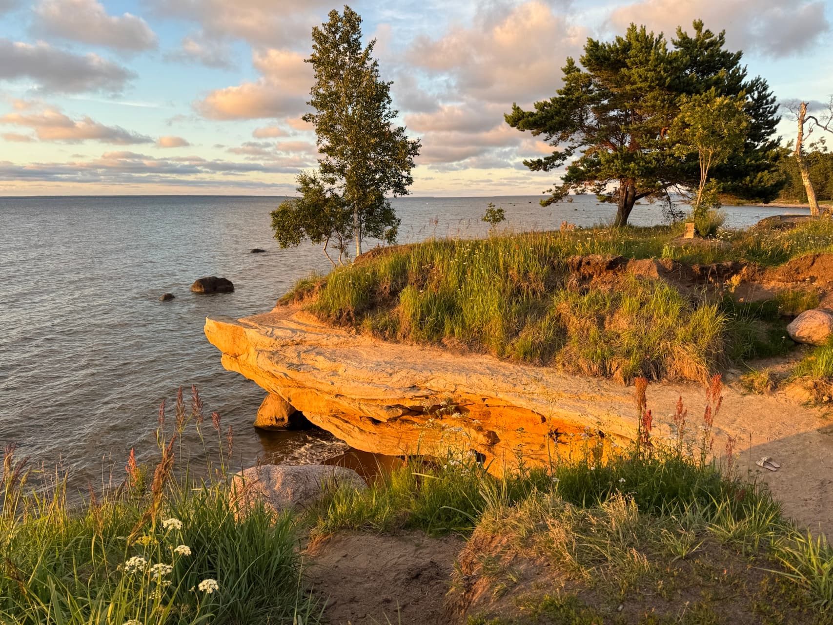 Golden cliff edge meets calm, grey sea water under a sunset sky